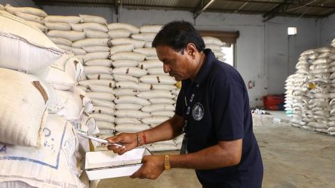 Un homme avec un carnet et un stylo devant des sacs de grains en toile