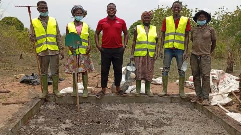 Des personnes avec des gilets jaunes et des outils de jardin debout devant une fosse à compost